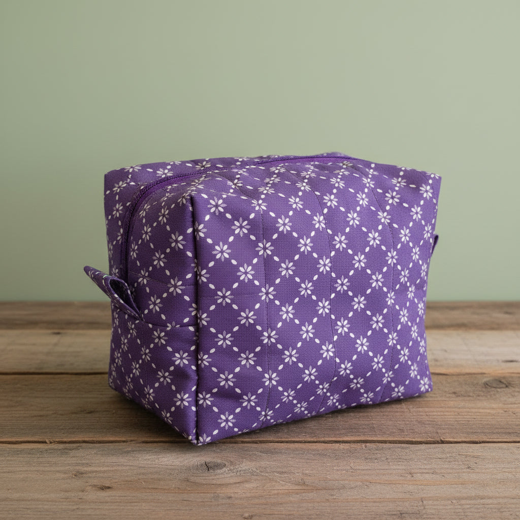 A purple and white patterned mini cosmetic bag with purple zipper, sitting a on rustic board with a sage green background