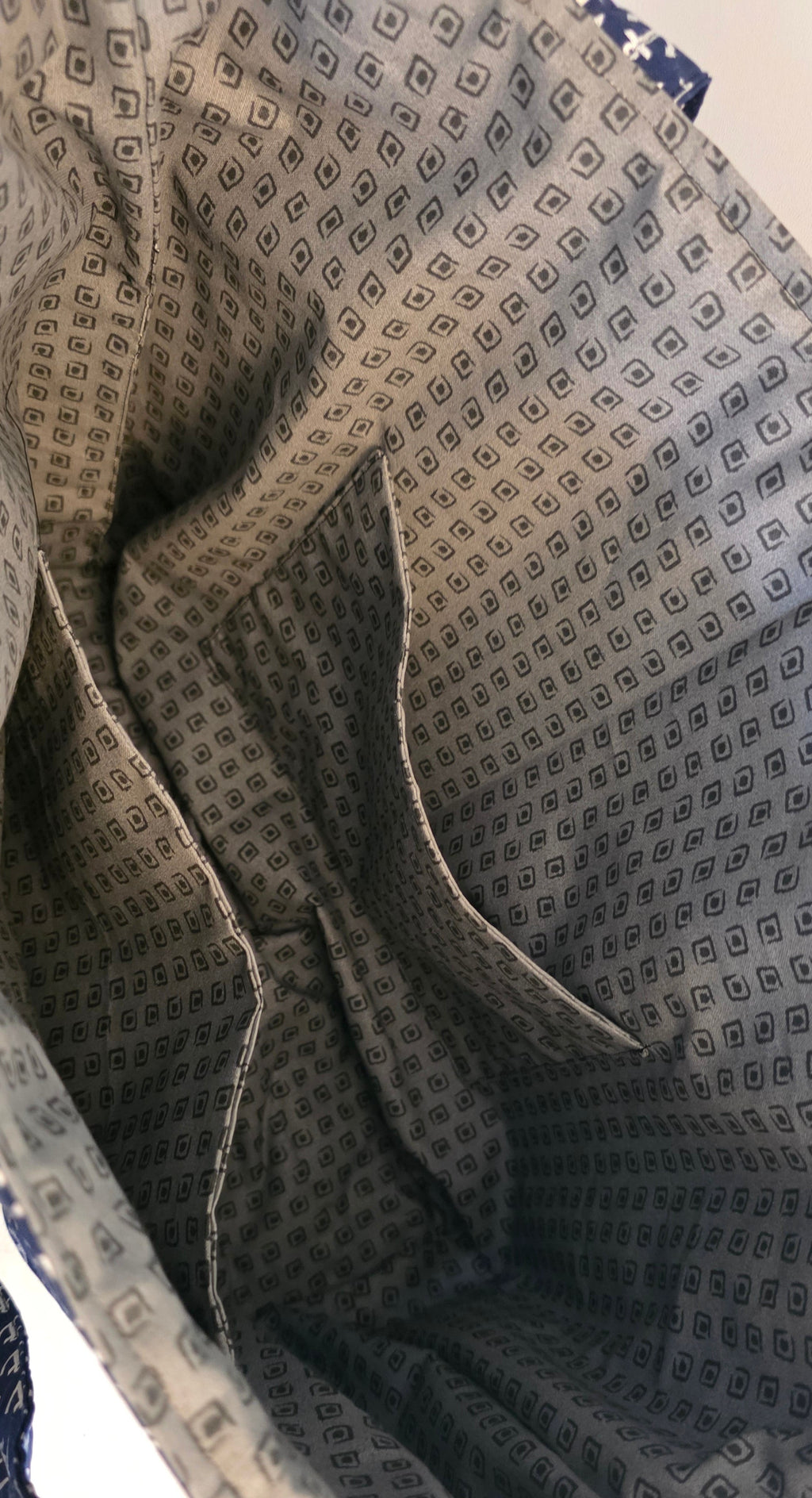 Close-up of the interior lining of a tote bag, showing a gray and black geometric patterned fabric with multiple dual compartments.