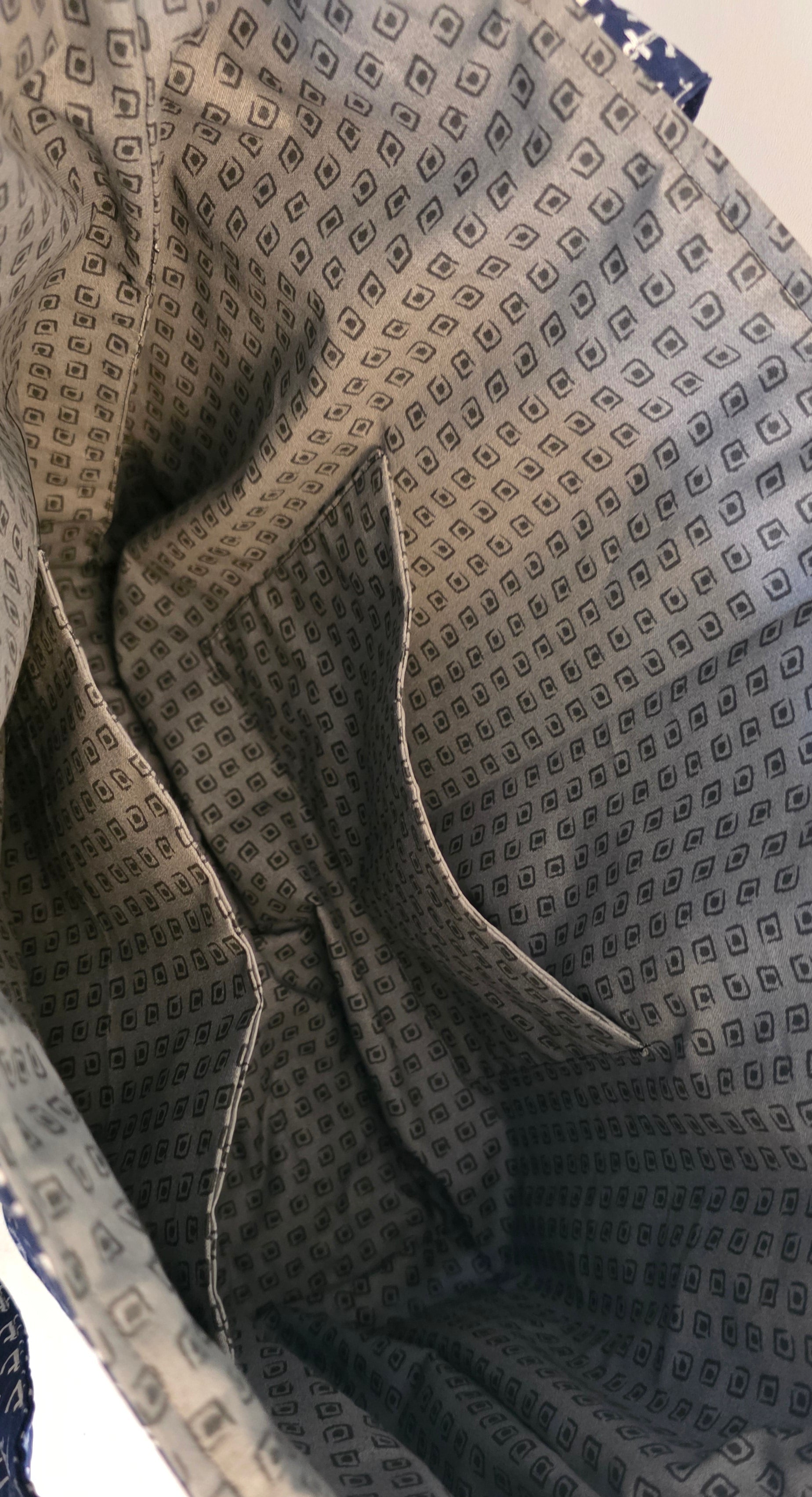 Close-up of the interior lining of a tote bag, showing a gray and black geometric patterned fabric with multiple dual compartments.