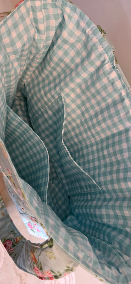 Close-up of a fabric storage basket or organizer with a light blue and white gingham pattern lining and a floral-patterned fabric side.