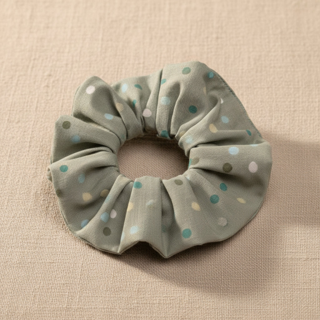 Top-down view of sage green cotton scrunchie showing ruched texture and dot pattern