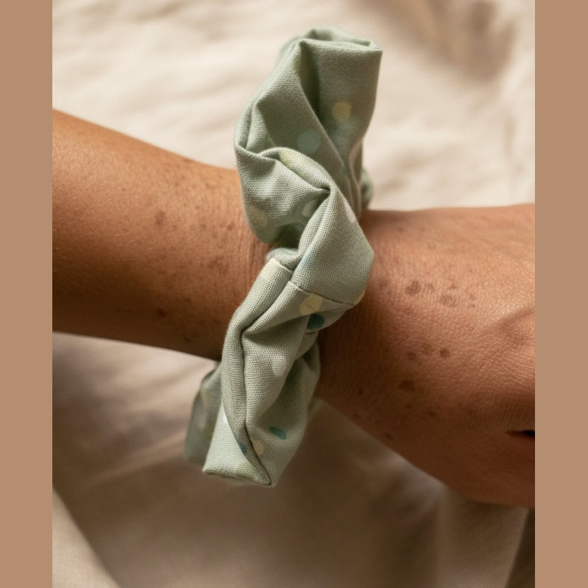 Sage green dotted scrunchie worn as a wrist bracelet on freckled skin