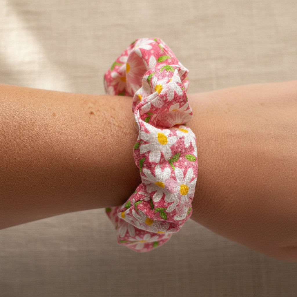Pink daisy scrunchie worn as a wrist accessory on freckled skin