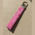 Pink watercolor keychain with silver clasp and split ring against warm fabric linen