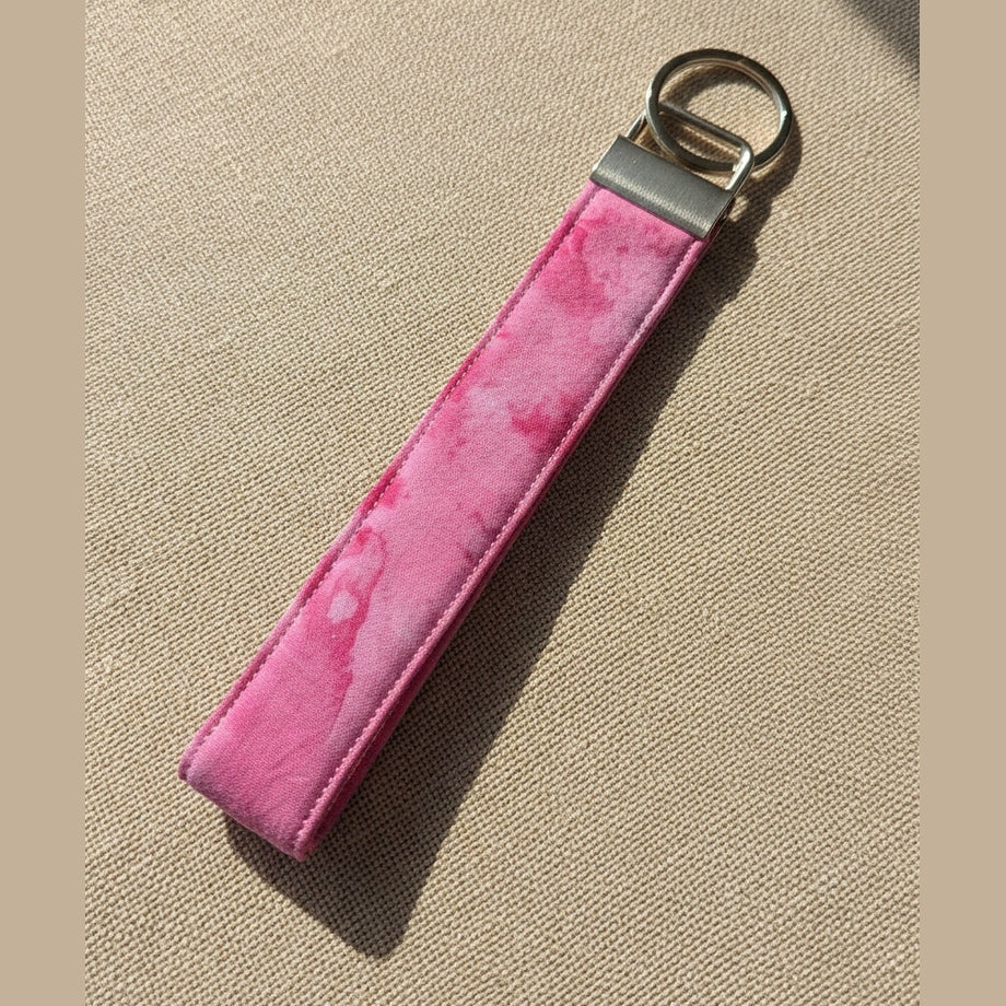 Pink watercolor keychain with silver clasp and split ring against warm fabric linen