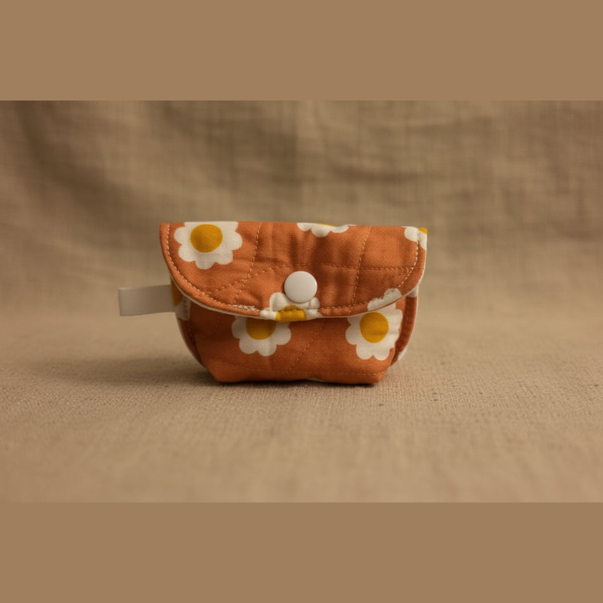 An orange quilted pouch with a white and yellow daisy pattern, featuring a white snap button closure