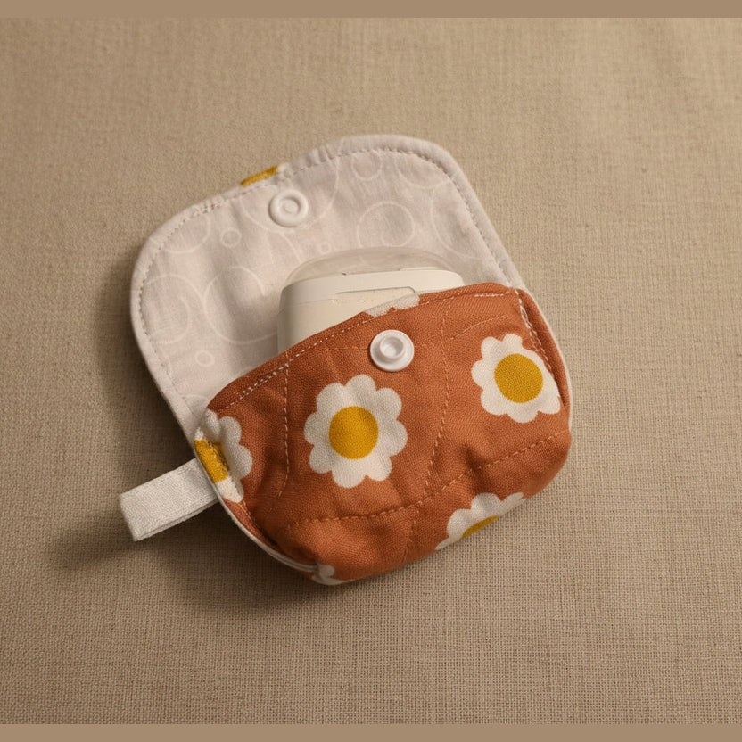 A close-up of a reusable cloth diaper or insert pouch with a white textured inner lining and a brown front pocket printed with white daisies that have yellow centers. 
