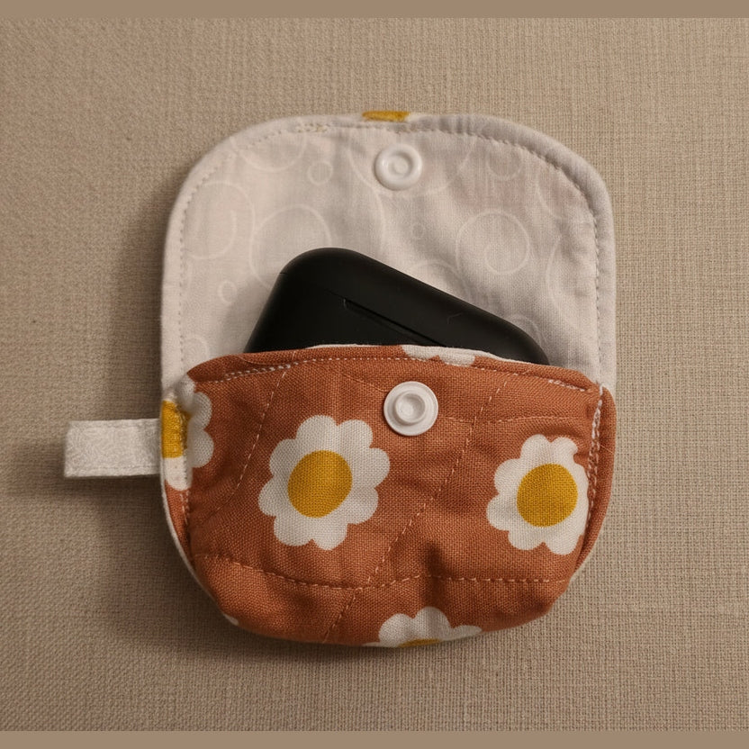 A small fabric pouch with a brown front pocket printed with white daisies and yellow centers, shown open with a white interior and a black item partially tucked inside, on a plain light background.