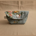 A small fabric pouch with a floral print in light blue, pink, and yellow, featuring a snap button closure, shown on a light beige surface.