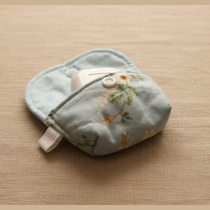 A light blue quilted fabric pouch with a floral print, featuring a front pocket holding a white mouse, photographed on a plain beige surface.