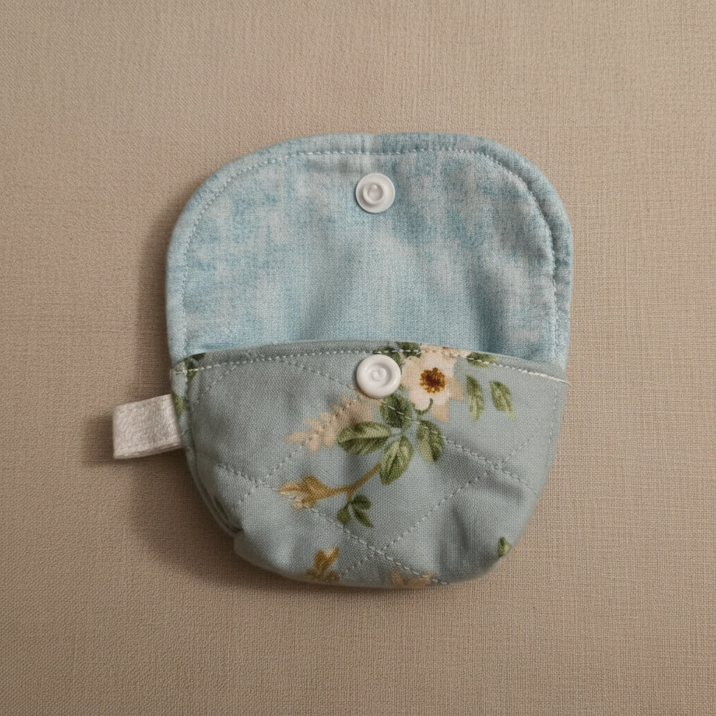 A light blue quilted fabric pouch with a floral print and snap-button closure