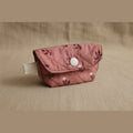 A small quilted fabric pouch in dusty rose pink with a dark floral pattern and a silver snap button closure, resting on a light-colored surface.