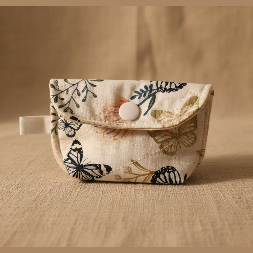 A small fabric pouch with a snap button closure, featuring a cream-colored background with a butterfly pattern in navy blue, orange, and gold.