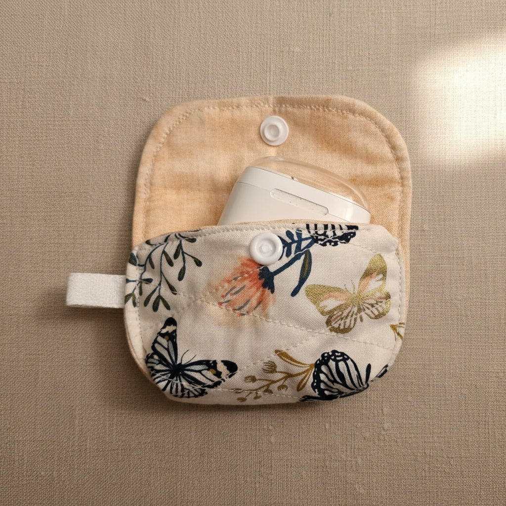 A small fabric pouch or case with a floral and butterfly print, holding a white oval item, photographed on a plain light beige background.