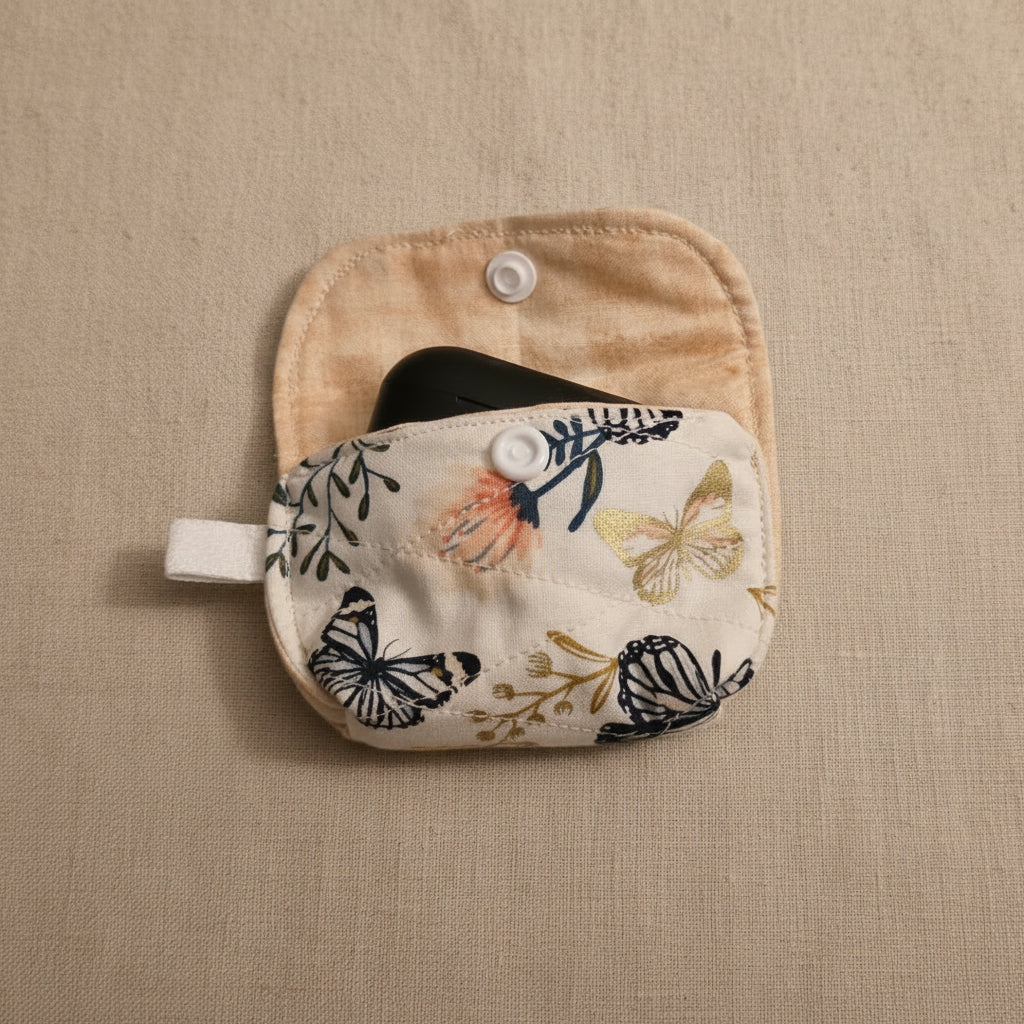 A small fabric pouch with a snap-button closure, featuring a cream-colored front pocket with a butterfly and floral print.
