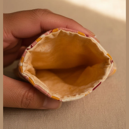 A close-up of a hand holding the open end of a small fabric pouch or bag, showing an orange interior lining and a patterned exterior edge with pink, yellow, and white tones.