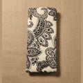 A folded fabric item, likely a yoga mat or towel, featuring a black paisley pattern on a cream background, displayed against a plain beige wall.