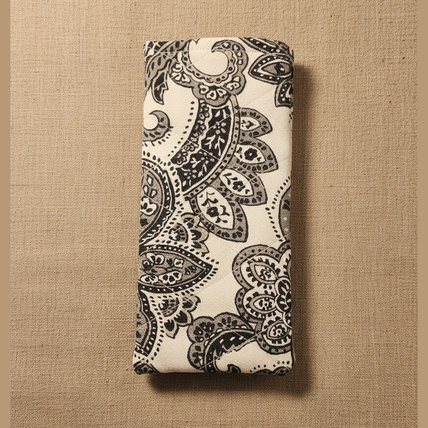 A folded fabric item, likely a yoga mat or towel, featuring a black paisley pattern on a cream background, displayed against a plain beige wall.