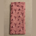 A pink quilted fabric pouch or sleeve with a dark floral pattern, hanging on a plain beige wall above a gray textured surface.
