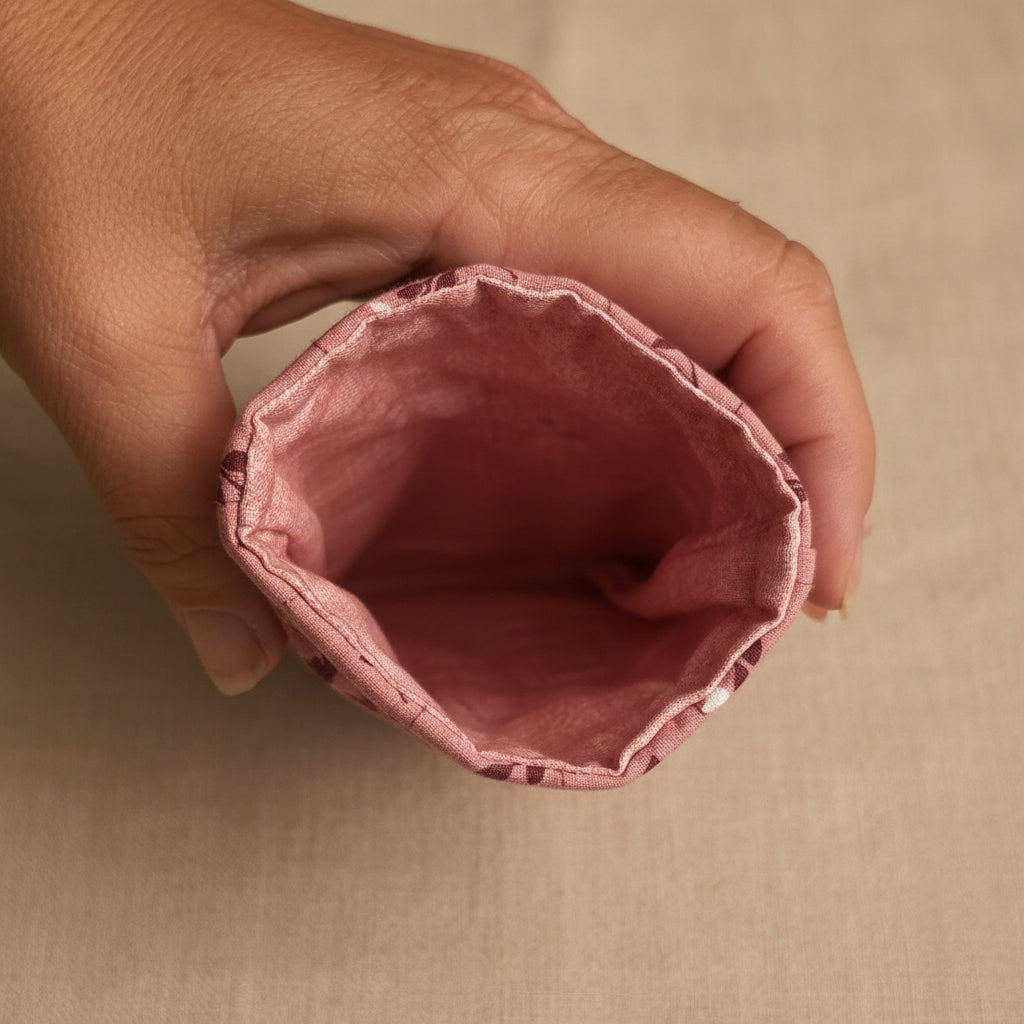 A close-up of a hand holding the open end of a dusty rose pink fabric pouch or sleeve, showing the stitched interior against a light background.