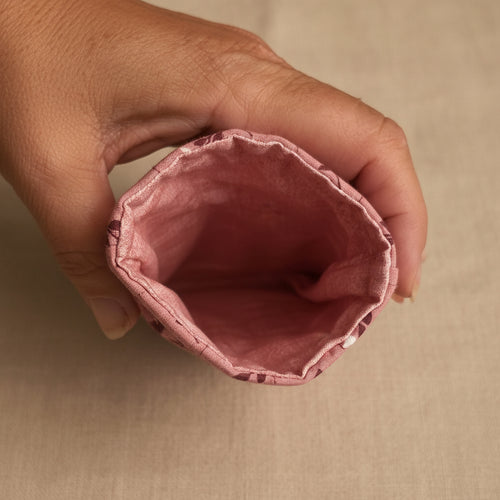 A close-up of a hand holding the open end of a dusty rose pink fabric pouch or sleeve, showing the stitched interior against a light background.