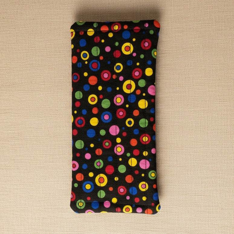 A rectangular black fabric pouch or sleeve with a colorful retro concentric circle dot pattern, hanging against a plain beige wall.