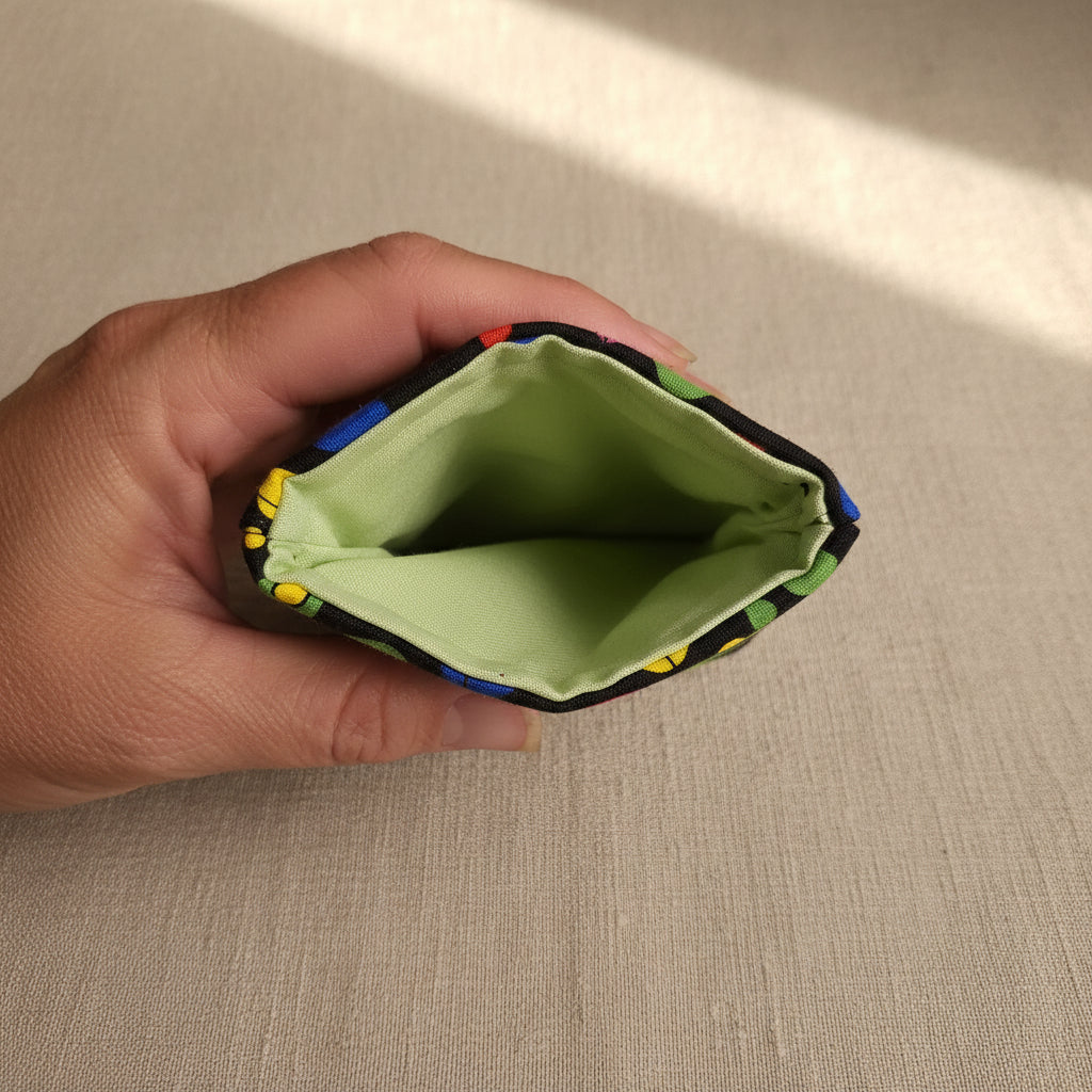 A close-up of a hand holding the open end of a small fabric pouch or sleeve, showing a light green interior lining and a multicolored patterned exterior edge.