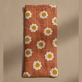A dusty pink quilted fabric pouch or sleeve with a white daisy pattern, hanging against a plain beige wall.