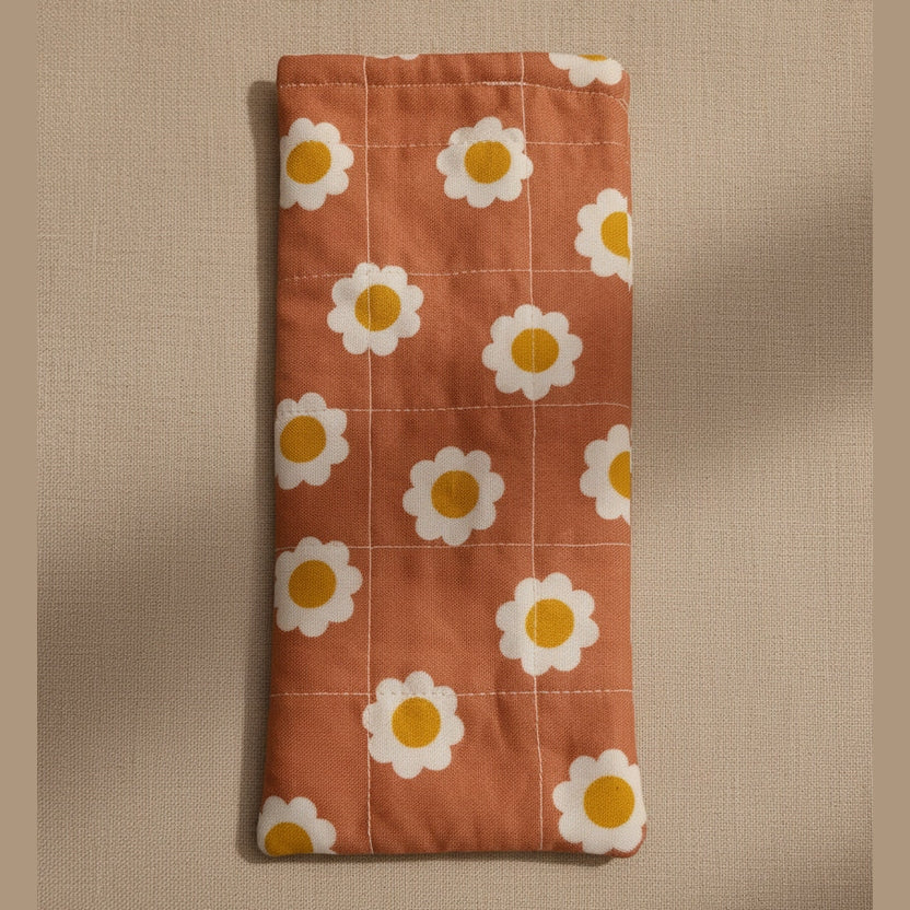A dusty pink quilted fabric pouch or sleeve with a white daisy pattern, hanging against a plain beige wall.