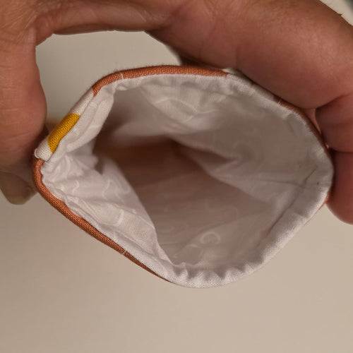 A close-up of a hand holding the opening of a small pouch or sleeve, showing a white interior lining..