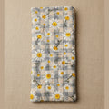 A rectangular fabric item, likely a pouch or sleeve, featuring a daisy and plaid pattern in gray, white, and yellow, photographed against a plain beige background.