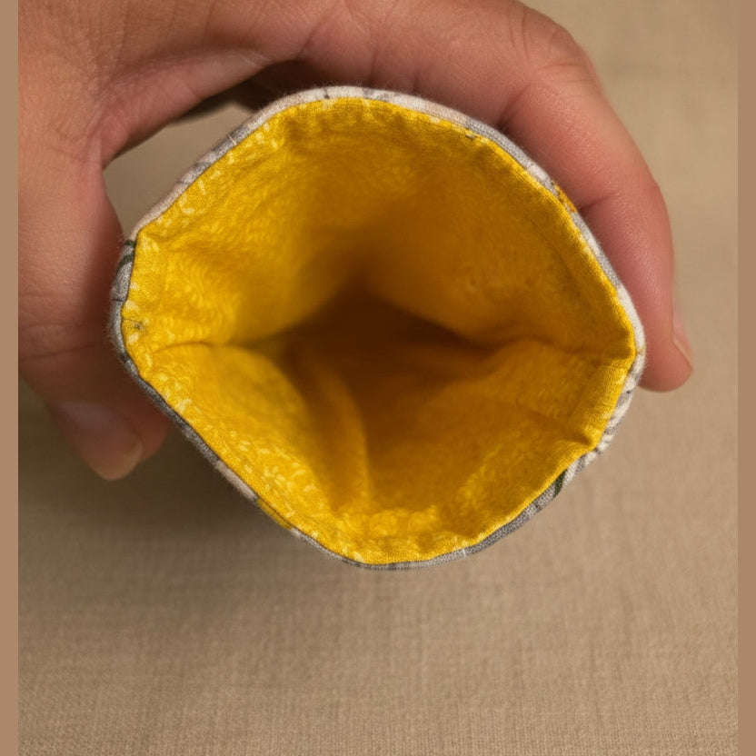 A close-up of a hand holding the open end of a gray fabric pouch or sleeve, showing a bright yellow textured lining inside.