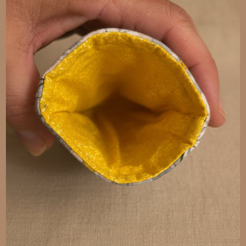 A close-up of a hand holding the open end of a gray fabric pouch or sleeve, showing a bright yellow textured lining inside.