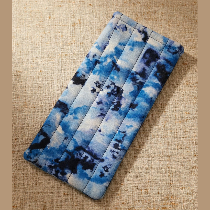 A rectangular zippered pouch with a blue and white tie-dye pattern, shown against a plain beige wall.