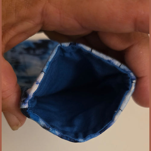 A close-up of a hand holding the open end of a small fabric pouch or sleeve, showing a blue patterned exterior and a solid dark blue interior against a plain light background.
