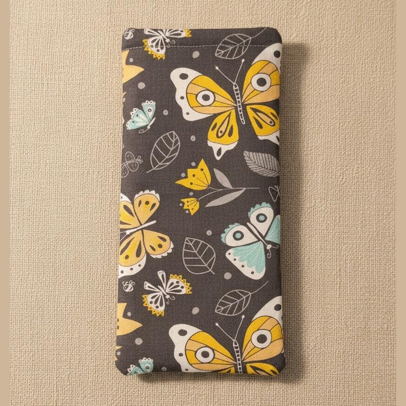 A rectangular fabric pouch or sleeve with a dark gray background and a colorful butterfly and leaf print in yellow, white, and light blue, shown against a plain beige background.