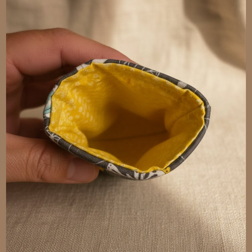 A close-up of a fabric pouch or bag being held by a hand, showing a bright yellow patterned lining and a gray patterned exterior.