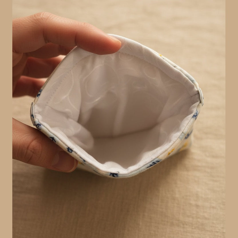 Close-up of the inside of a fabric pouch or sleeve, showing a white lining with a patterned fabric edge, held by a hand against a plain light background.