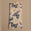 A rectangular quilted fabric pouch with a printed pattern of black and gold butterflies and small peach flowers on a cream background, shown against a plain beige wall.