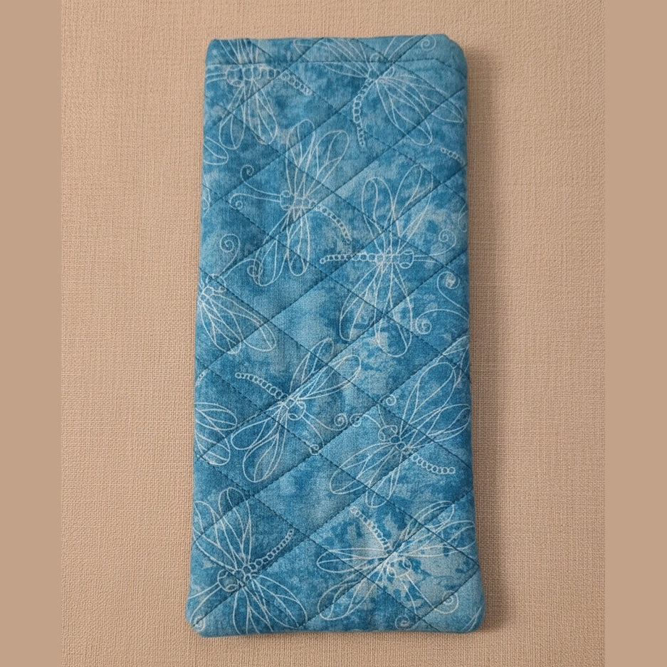 A blue quilted fabric pouch with a white dragonfly pattern, shown on a solid peach-colored background.