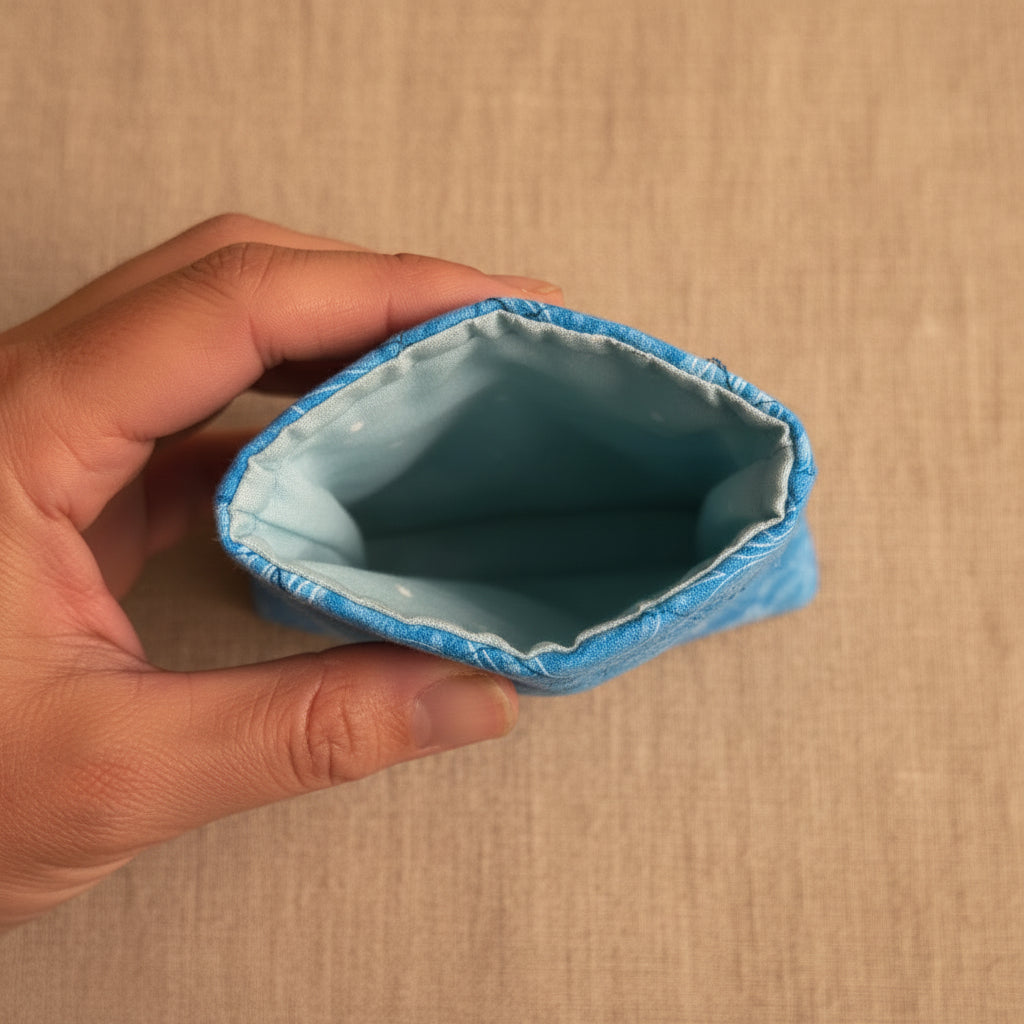 A close-up of a hand holding the open end of a light blue fabric pouch or sleeve, showing the stitched interior and blue trim against a plain light background.