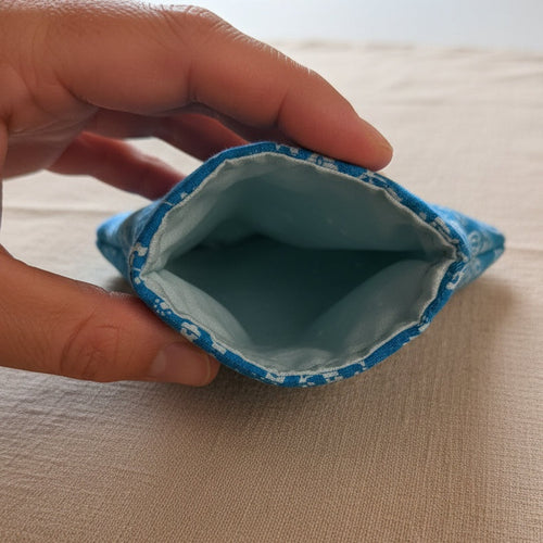 A close-up of a hand holding the open end of a cylindrical blue and white fabric item, showing the light blue interior lining.