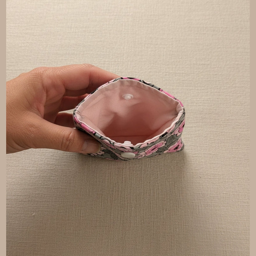 A close-up of a fabric pouch or sleeve being held by a hand, showing a pink interior lining and a patterned exterior with pink, black, and white tones.