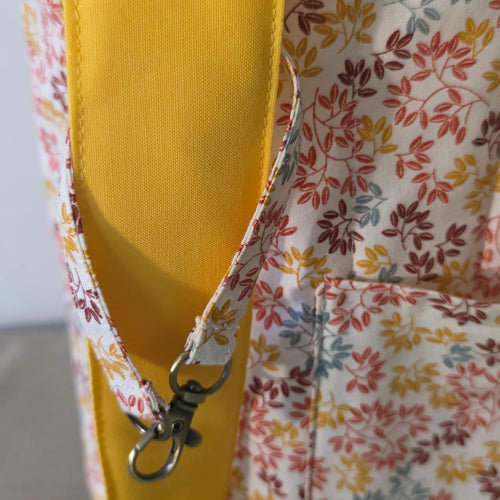 Close-up of a floral fabric bag or pouch with a yellow interior lining and a metal snap closure, shown against a plain light background.