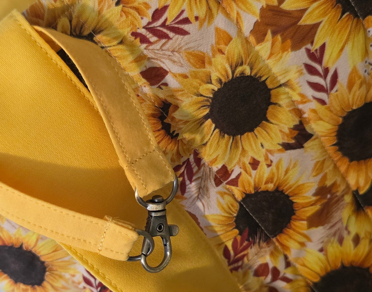 Close-up of a yellow fabric accessory with a sunflower print and a metal snap hook clasp