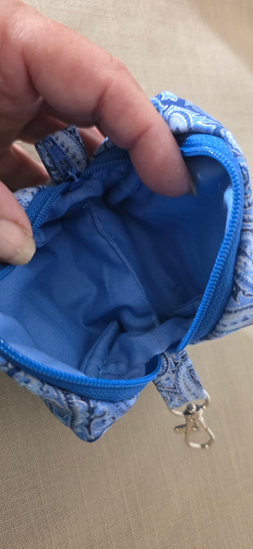 A close-up of a hand holding open a small zippered pouch with a blue and white paisley patterned exterior and a bright blue interior.