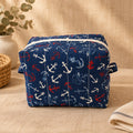 A rectangular fabric storage bag or organizer with a navy blue background and an anchor pattern in white and red, sitting on a beige fabric surface.