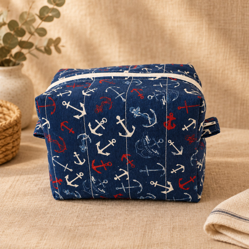 A rectangular fabric storage bag or organizer with a navy blue background and an anchor pattern in white and red, sitting on a beige fabric surface.