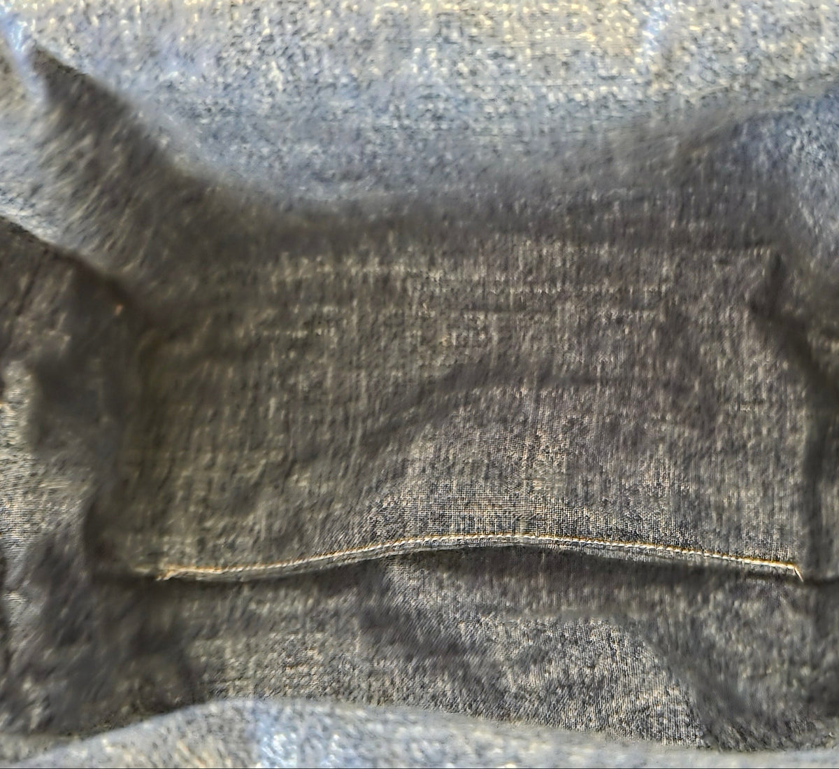 Close-up of the inside of a dark gray or charcoal denim bag, showing the texture of the fabric and a single row of light-colored contrast stitching.