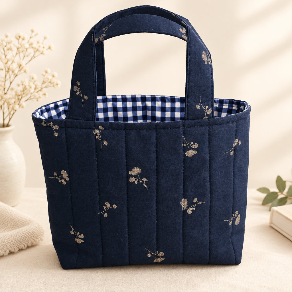 A navy-blue quilted fabric tote bag with a floral pattern and a blue-and-white gingham lining